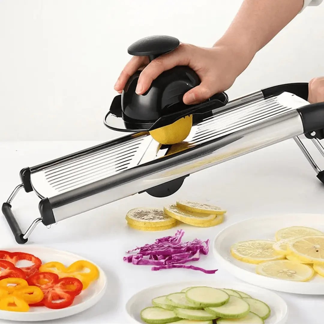 Hand using the mandoline slicer with hand guard to slice a lemon, sliced peppers and cucumber in front