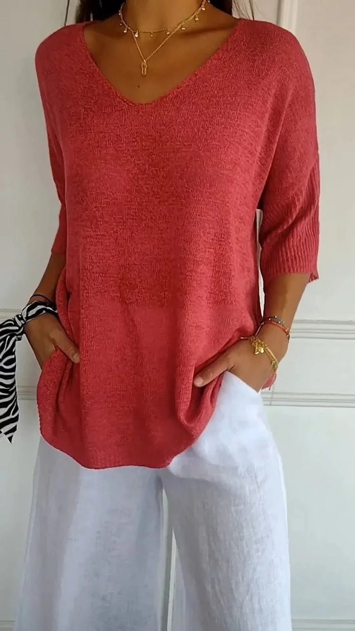 Women's red V-neck knit sweater worn with white trousers