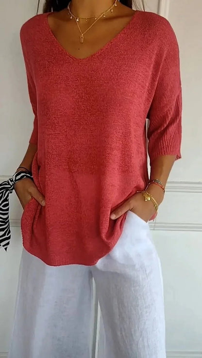 Women's red V-neck knit sweater worn with white trousers