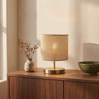 Natural fabric table lamp lit on a walnut sideboard