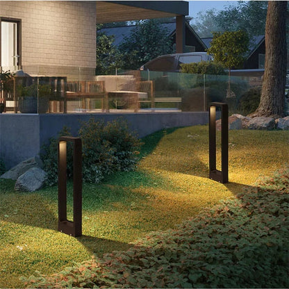 Two black bollard lights casting warm light across a lawn near a patio
