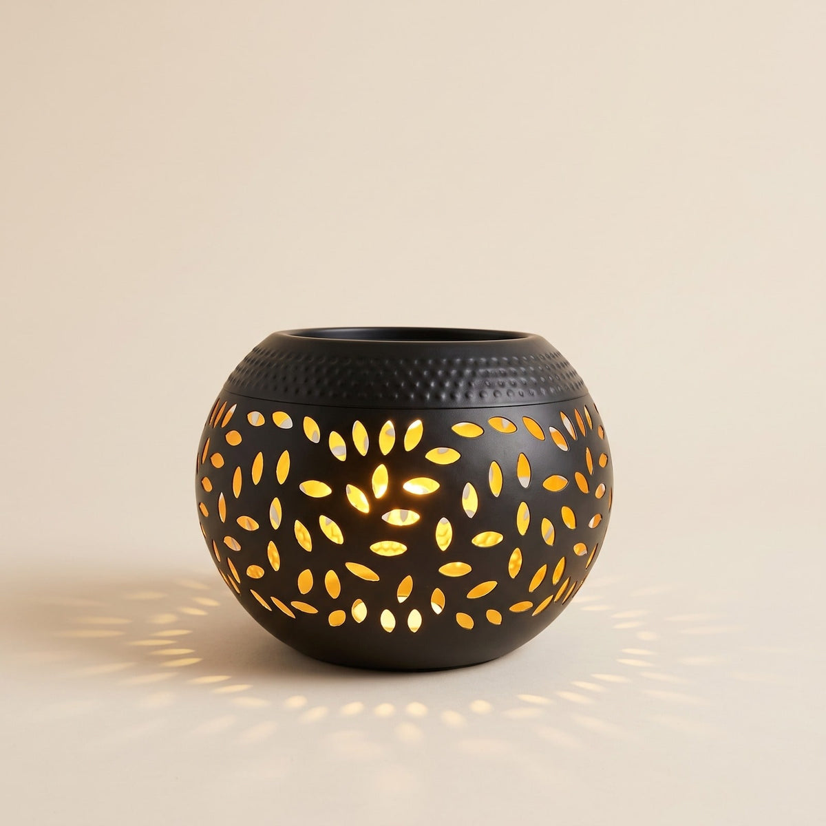 Black solar garden lantern with leaf cut outs glowing warm on a cream background