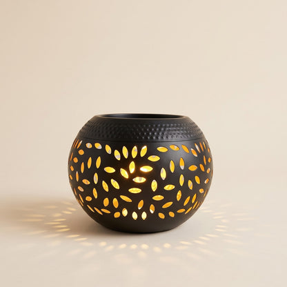 Black solar garden lantern with leaf cut outs glowing warm on a cream background