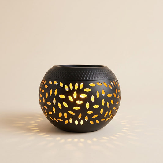 Black solar garden lantern with leaf cut outs glowing warm on a cream background