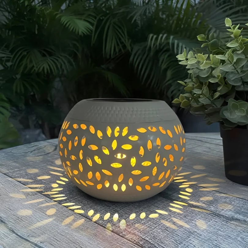 White solar garden lantern glowing through leaf shaped cut outs on an outdoor table