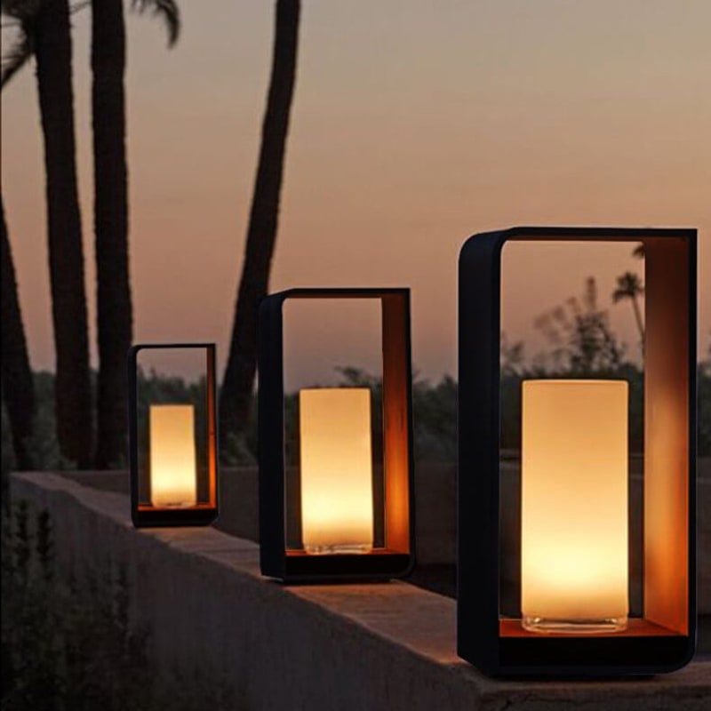 Three outdoor lanterns in small, medium and large on a low garden wall at sunset