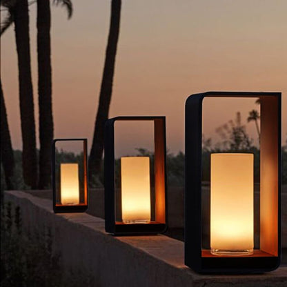 Three outdoor lanterns in small, medium and large on a low garden wall at sunset