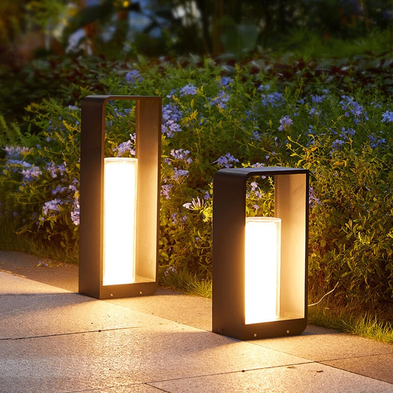 Two lit lanterns standing on a garden path in front of flowering plants