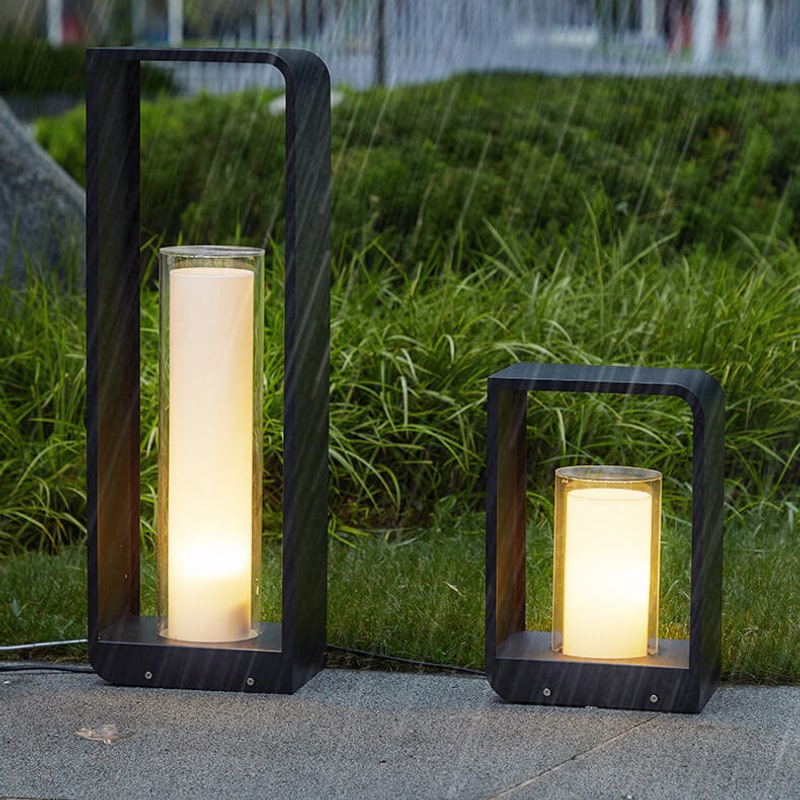 Large and small outdoor lanterns glowing in the rain beside a hedge