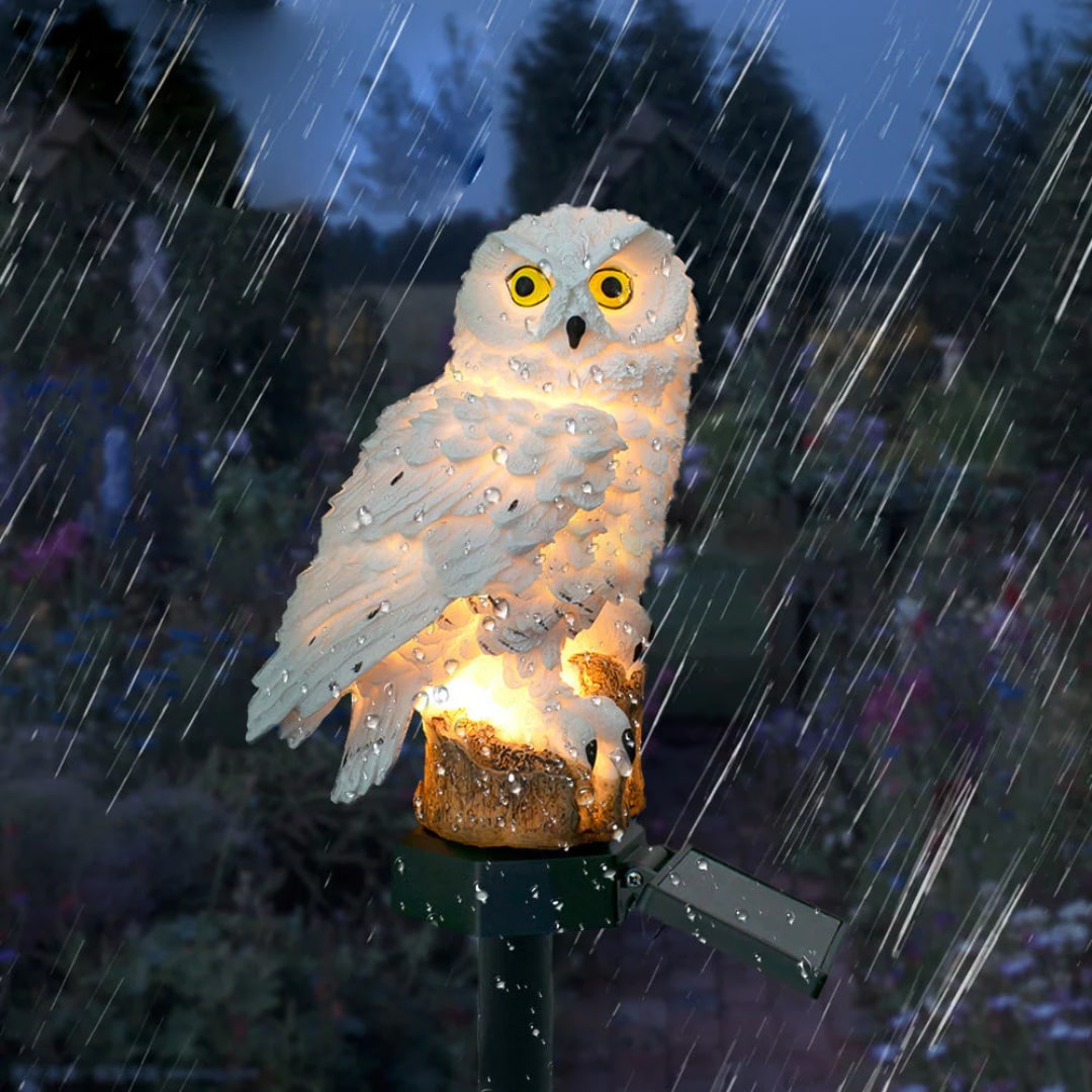 Solar owl garden light glowing in the rain in a flower bed