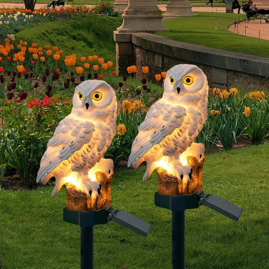 Set of two solar owl stake lights in a garden with tulips