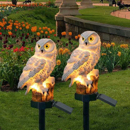 Set of two solar owl stake lights in a garden with tulips