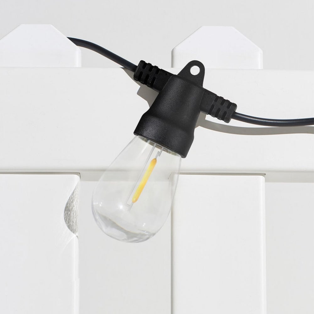 Clear Edison bulb hanging from a black socket on a white fence