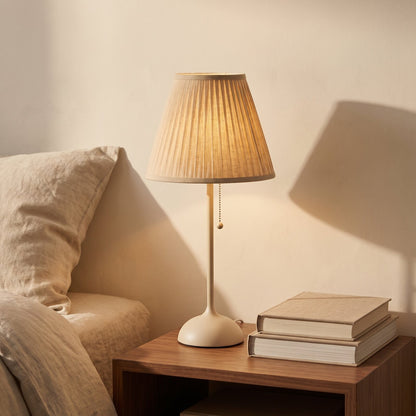 Pleated fabric table lamp lit on a walnut bedside table