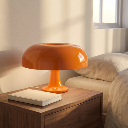 Orange mushroom dome table lamp lit on a walnut bedside table