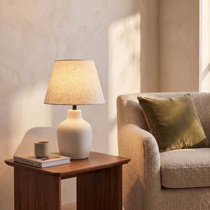 Speckled ivory ceramic table lamp lit on a walnut side table beside an armchair
