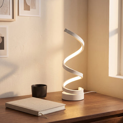 White spiral LED table lamp lit on a walnut desk in a home office
