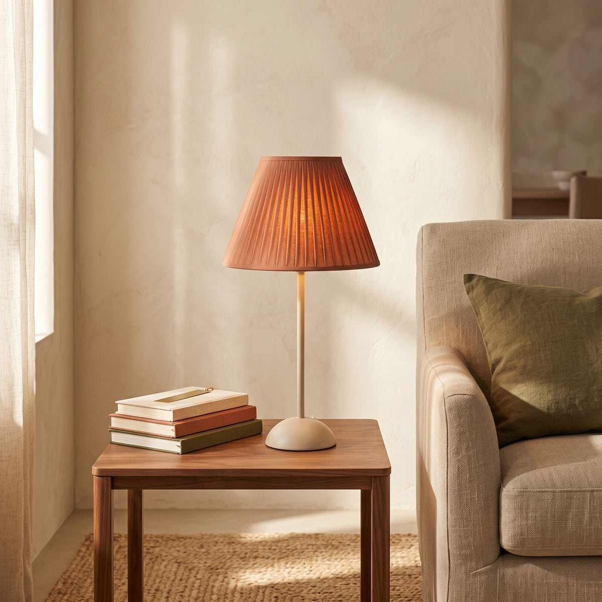 Terracotta pleated shade table lamp lit on a walnut side table beside an armchair